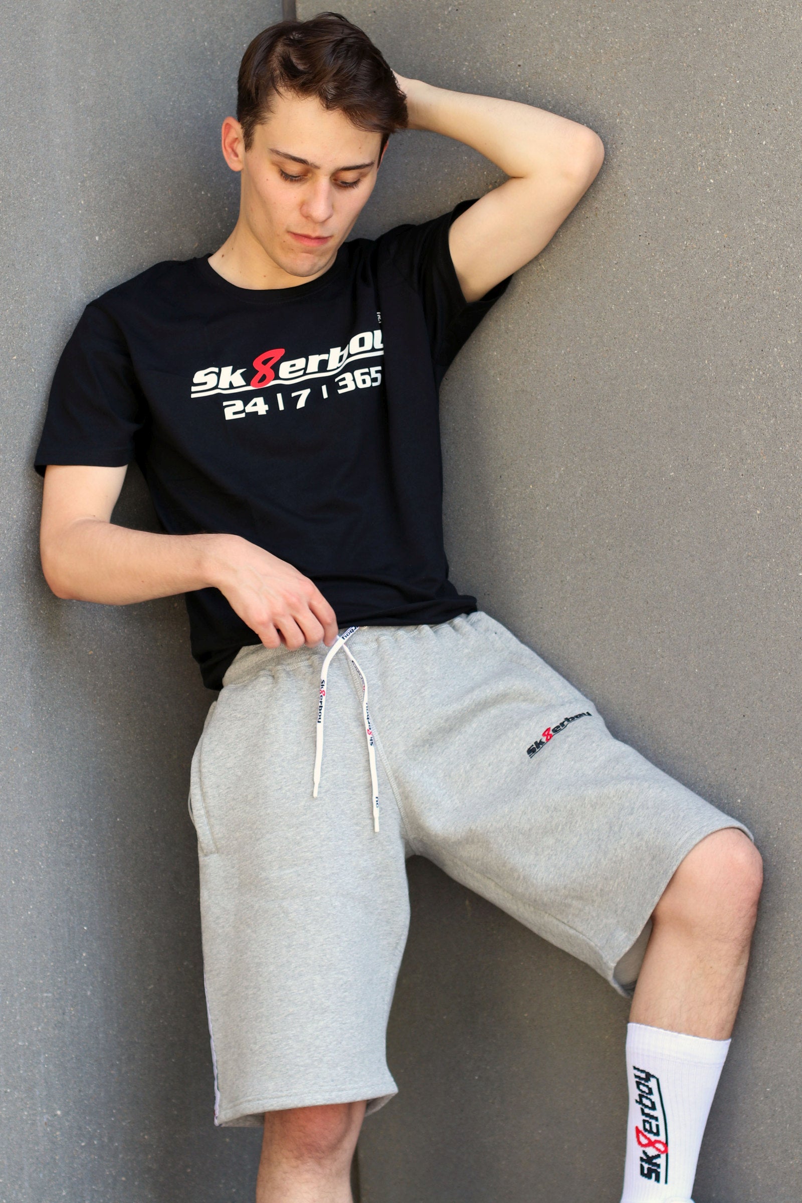 junger typ trägt grauen sk8erboy trainingsanzug in lang mit passender hose und 365 t-shirt zu seinen weißen nike sneaks