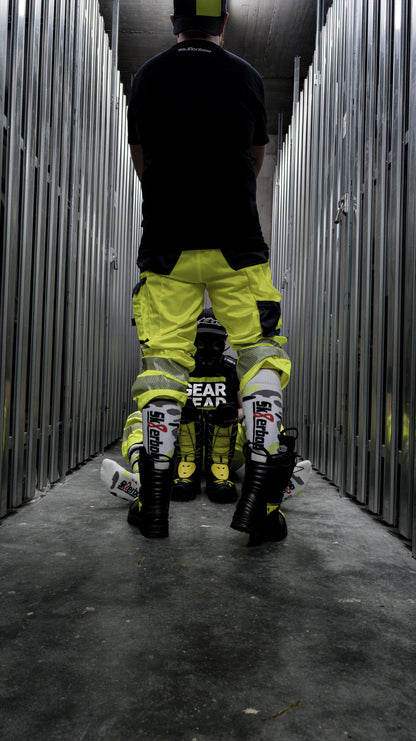 junger gear haed in neon gelben engelbert strauss dress mit boots und mx socks in neon gelb von sk8erboy von hinten in boots und weiterer gear head im hintergrund am boden sitzend