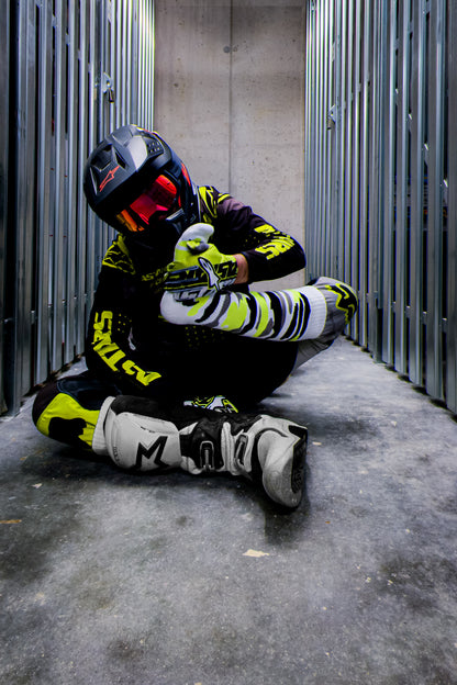 motocross biker in neon gelben dress mit cross boots und mx socks in neon gelb von sk8erboy von vorne am boden sitztend in den boots und sniffend