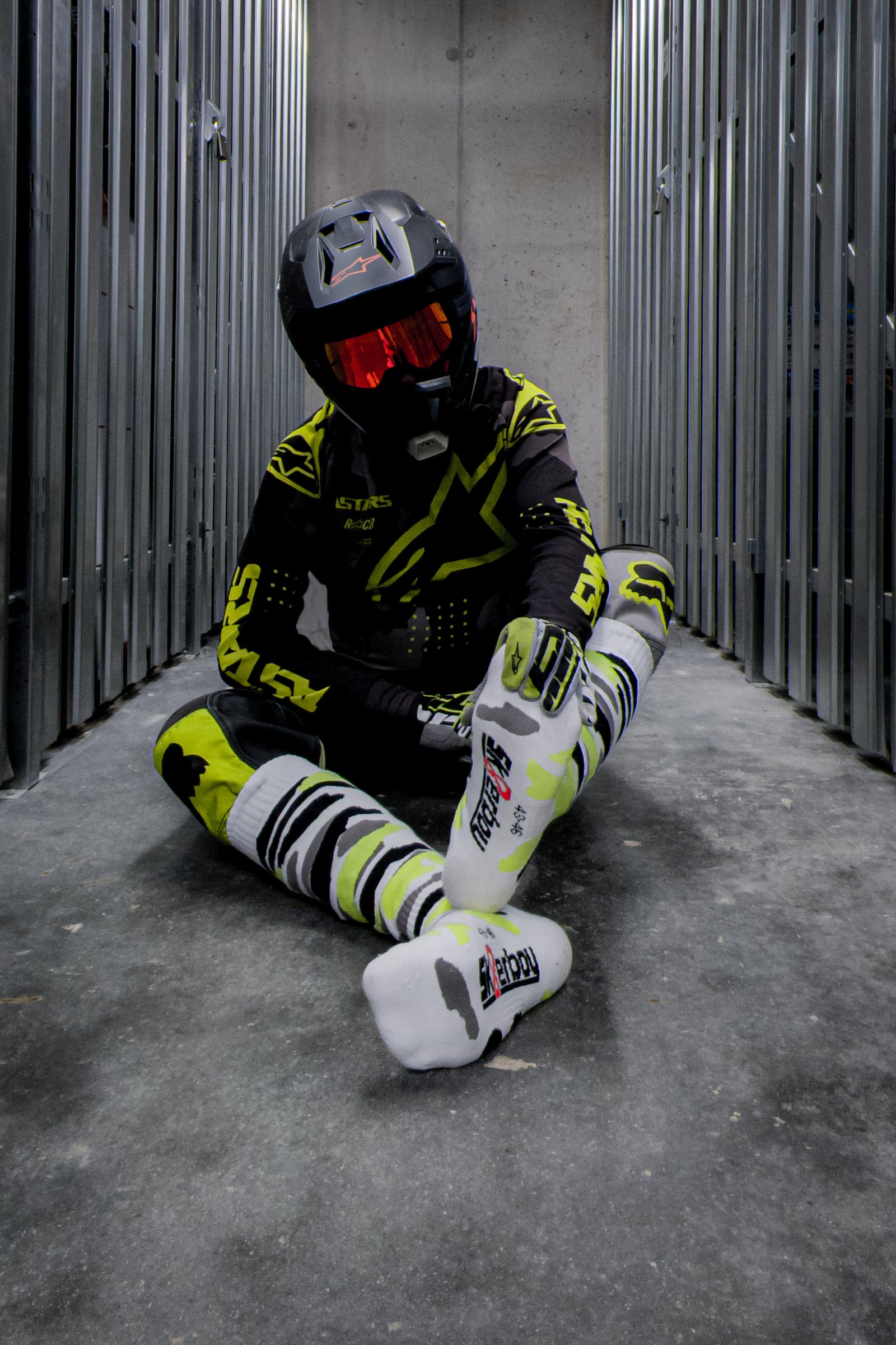 motocross biker in neon gelben dress mit cross boots und mx socks in neon gelb von sk8erboy von vorne am boden sitzend