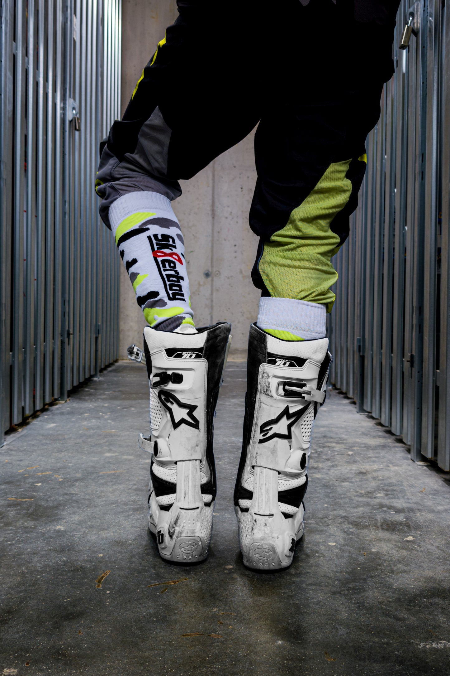 motocross biker in neon gelben dress mit cross boots und mx socks in neon gelb von sk8erboy von hinten in den boots mit logo auf der linken wade